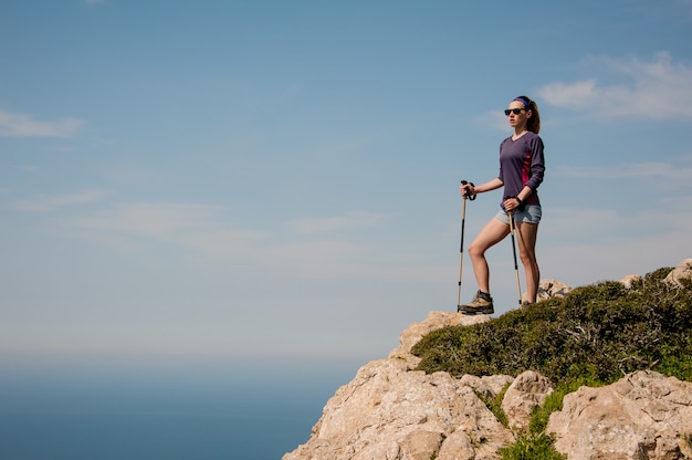 Junges Mädchen, das kurz gesagt auf dem Felsen mit Spazierstöcken steht