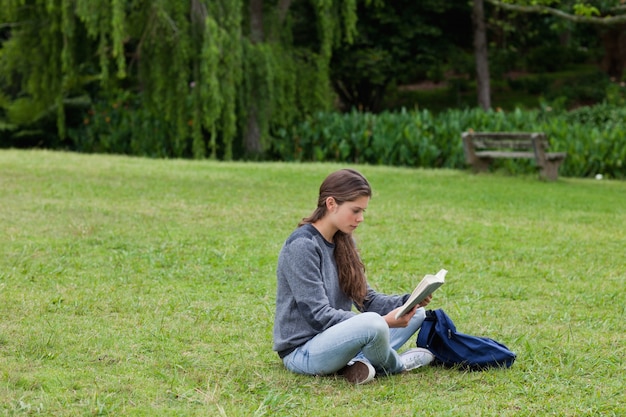 Junges Mädchen, das mit überkreuzten Beinen beim Lesen eines Buches sitzt