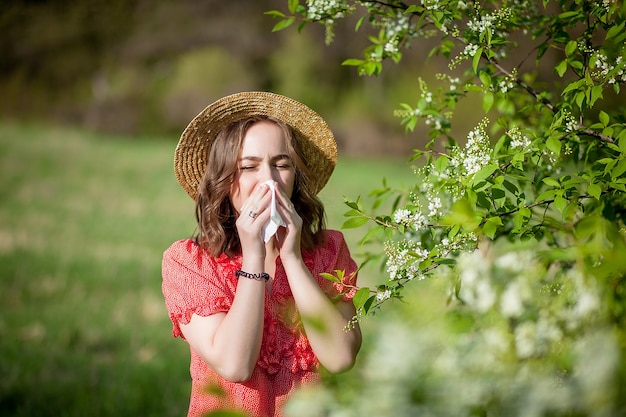 Junges Mädchen, das Nase bläst und im Gewebe vor blühendem Baum niest. Saisonale Allergene, die Menschen betreffen. Schöne Frau hat Rhinitis.