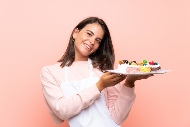 Junges Mädchen, das viele verschiedene Minikuchen über lokalisierter Wand hält