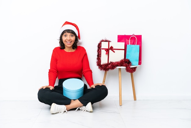 Junges Mädchen, das Weihnachten feiert, das auf dem Boden lokalisiert auf weißem Hintergrund mit überraschtem Gesichtsausdruck sitzt