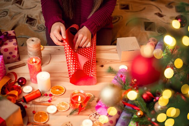 Junges Mädchen, das Weihnachtsgeschenke mit Dekorationen auf dem Tisch verpackt
