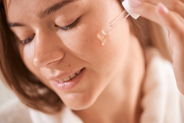 Junges Mädchen, das zu Hause Vitamine auf sein Gesicht aufträgt Hautpflegekonzept