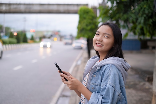 Junges Mädchen des Porträtlächelns benutzen Handy auf Straßenhintergrund.