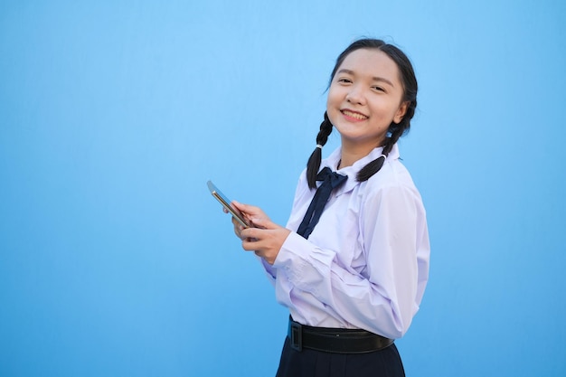 Junges Mädchen des Studenten, das intelligentes Telefon auf blauem Hintergrund verwendet