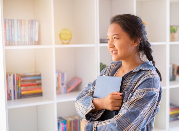 Junges Mädchen des Studenten halten Laptop auf BücherregalhintergrundAsiatisches Mädchen