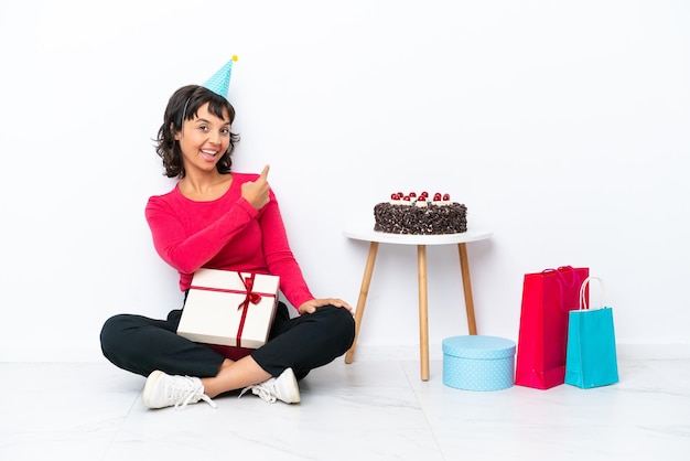 Junges Mädchen feiert seinen Geburtstag auf dem Boden sitzend isoliert auf weißem Hintergrund nach hinten zeigend