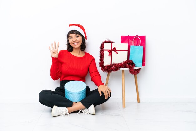 Junges Mädchen feiert Weihnachten auf dem Boden isoliert auf weißem Hintergrund glücklich und zählt vier mit den Fingern