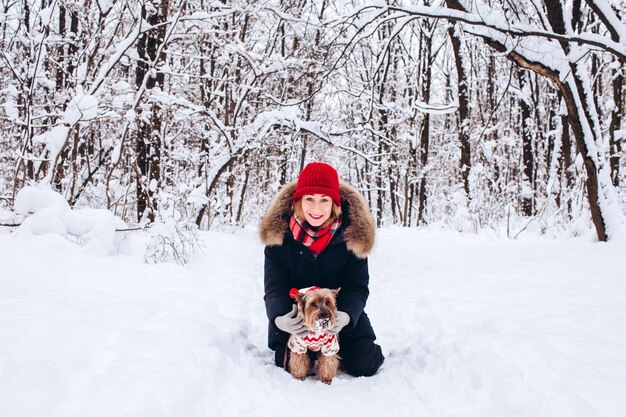 Junges Mädchen geht in den unteren Wäldern im Winter mit Hund, der einen Weihnachtspullover trägt