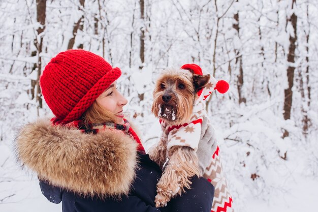 Junges Mädchen geht in den unteren Wäldern im Winter mit Hund, der einen Weihnachtspullover trägt