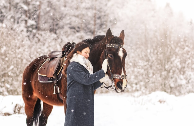 Junges Mädchen geht mit einem Pferd im Wald im Winter