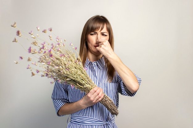 Junges Mädchen hält einen Strauß Wildblumen auf einem hellen Hintergrund, der eine Allergie gegen Blumen leidet