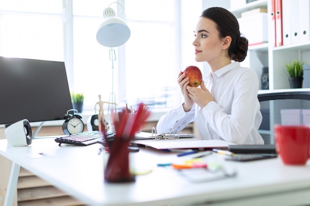 Junges Mädchen im Büro, das mit Dokumenten arbeitet und einen Apfel hält.