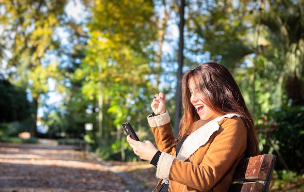 Junges Mädchen im Park im Herbst ist begeistert von einer Nachricht, die sie auf ihrem Smartphone erhalten hat.