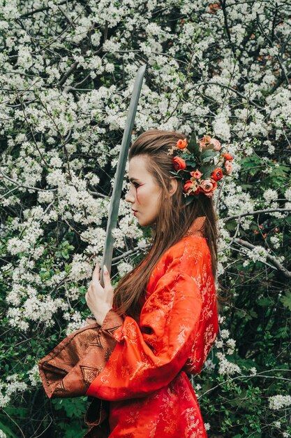 Junges Mädchen im traditionellen Kimano in einem blühenden Garten mit japanischem Samurai-Schwert Katana im Bild der Kriegerfrau