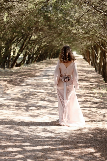 Junges Mädchen im Wald in einem langen Vintage-Kleid, das mit ihrem Rücken steht.