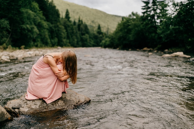 Junges Mädchen in der Depression, die am Stein im Fluss sitzt