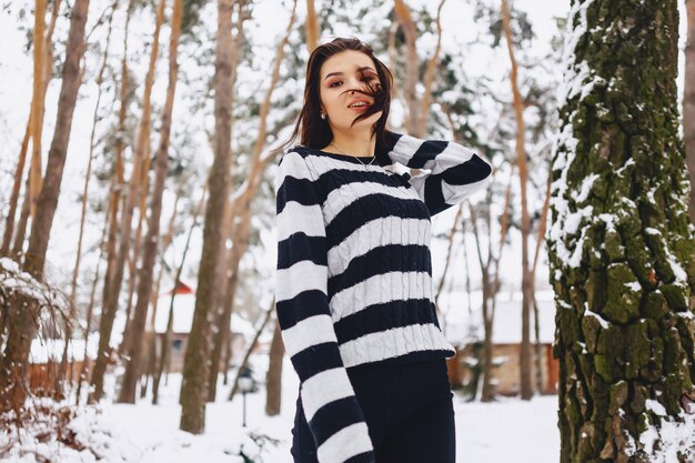 Junges Mädchen in der Schwarzweiss-Strickjacke in der Kälte am Wald unter den Kiefern