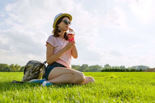 Junges Mädchen in der Sonnenbrille und im Hut trinkt Sommerbeerengetränk