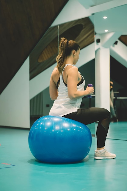 Junges Mädchen in der Sportklage tut körperliche Übungen mit Hanteln und einem Sitzball an der Turnhalle