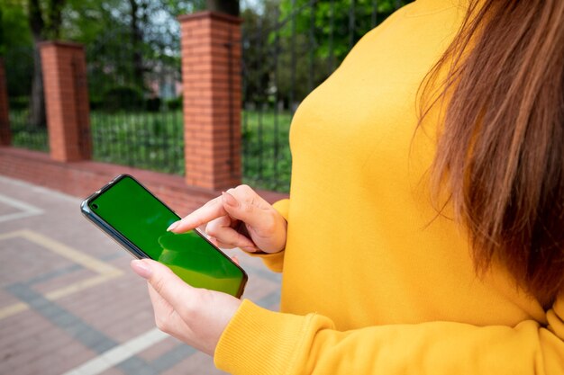 Junges Mädchen in einem gelben Pullover hält ein Smartphone auf der Straße