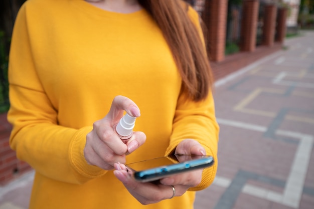 Junges Mädchen in einem gelben Pullover hält ein Smartphone auf der Straße