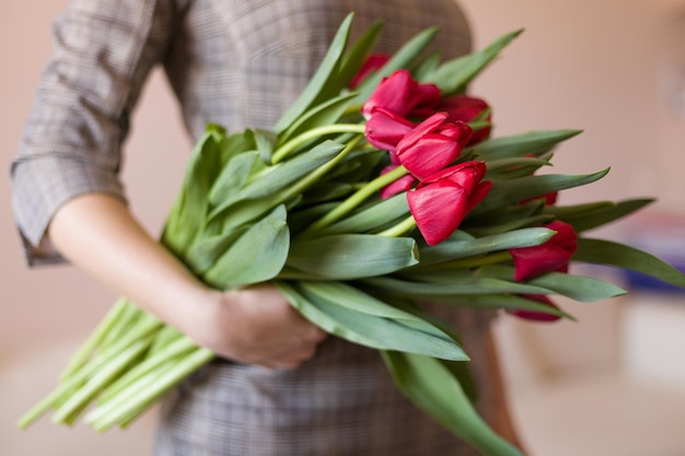 Junges Mädchen in einem Kleid, das einen Strauß leuchtend roter Frühlingsblumen hält