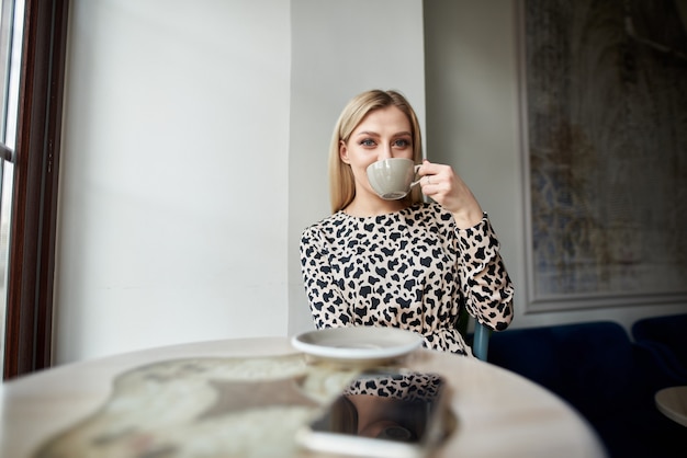 Junges Mädchen in einem Kleid mit einer Tasse Cappuccino in einem Café, das bereit ist, heißen Kaffee in einem Café zu trinken