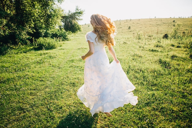 Junges Mädchen in einem weißen Kleid in der Wiese. Frau in einem schönen langen Kleid, das im Garten aufwirft