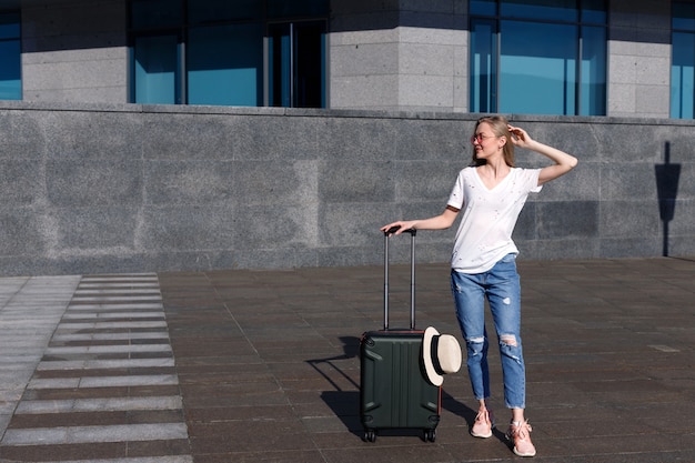 Junges Mädchen in einem weißen T-Shirt mit Gepäck in der Nähe eines Fußgängerüberwegs im Sommer auf einer Reise