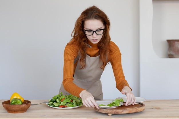 Junges Mädchen in einer Schürze macht in ihrer Küche einen gesunden Salat aus Gemüse und Kräutern