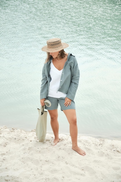 Junges Mädchen in natürlicher Leinenkleidung und einem Strohhut barfuß an einem weißen Sandstrand mit einem Leinen