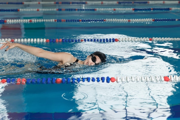 Junges Mädchen in Schutzbrille und Kappe, das Schmetterlingsstil im blauen Wasserbecken schwimmt