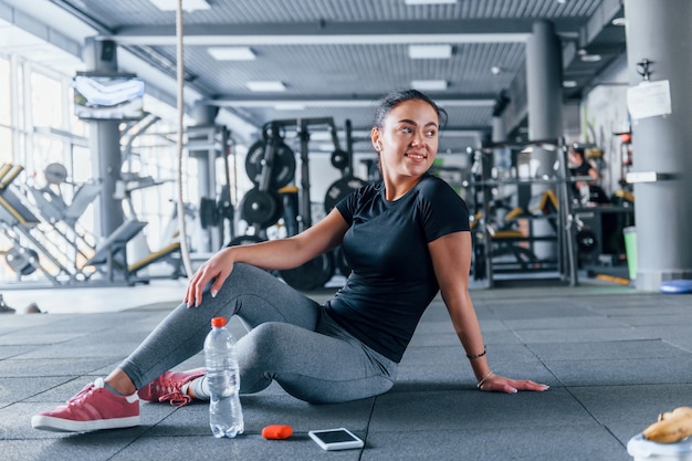 Junges Mädchen in sportlicher Kleidung, das eine Pause mit Essen und Wasser macht, ist tagsüber im Fitnessstudio.