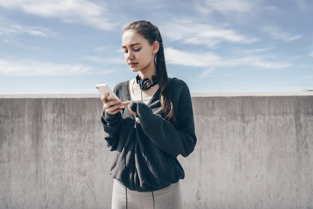 Junges Mädchen in stylischer schwarzer Kleidung schaut nach dem Training ins Smartphone