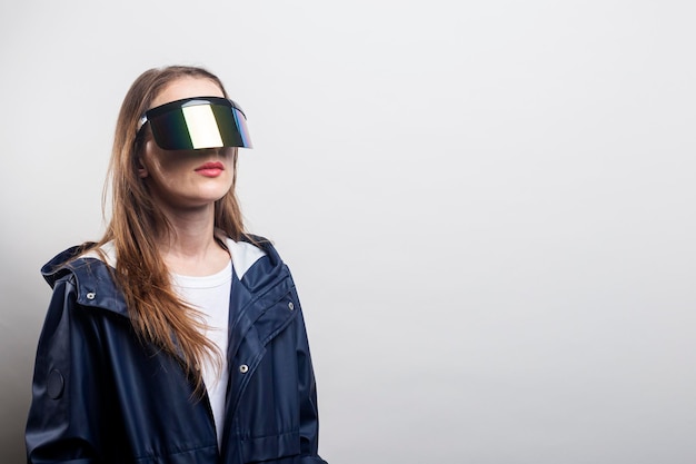 Junges Mädchen in Virtual-Reality-Brille in einer blauen Jacke auf hellem Hintergrund