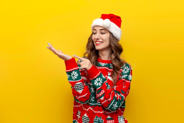 Junges Mädchen in Weihnachtspullover und Weihnachtsmannmütze hält leere Hände vor sich