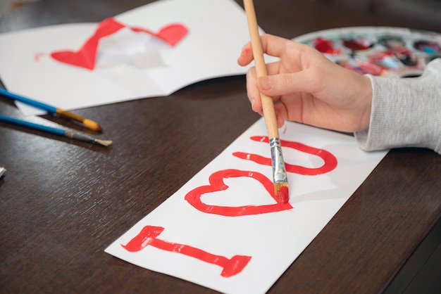 Junges Mädchen malen Ich liebe dich mit roter Farbe auf weißem Papier. Nahaufnahme von Valentinstag Grußkarte erstellen.