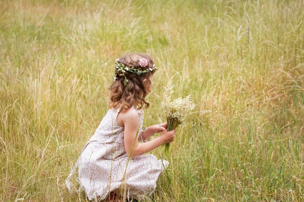 Foto junges mädchen mit blumen im haar, das wilde blumen auf einer wiese pflückt