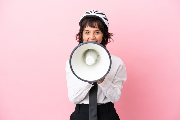 Junges Mädchen mit einem Fahrradhelm isoliert auf rosa Hintergrund, der durch ein Megaphon schreit