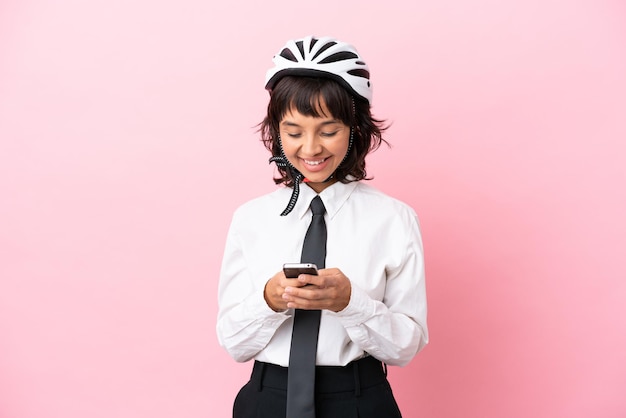 Junges Mädchen mit einem Fahrradhelm isoliert auf rosa Hintergrund, der eine Nachricht mit dem Handy sendet