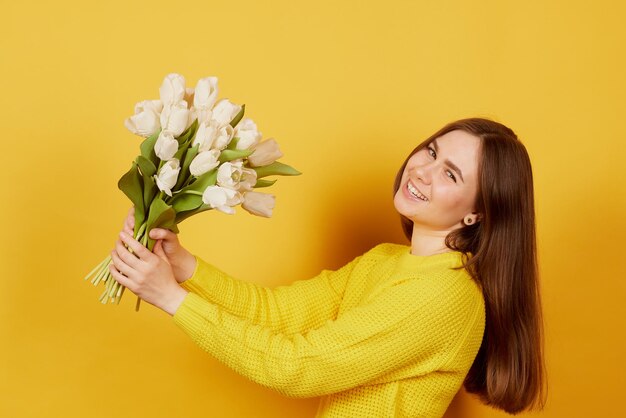 Junges Mädchen mit einem Strauß weißer Tulpen auf gelbem Hintergrund