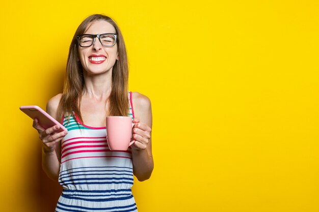 Junges Mädchen mit einem Telefon blinzelt und hält eine Tasse Kaffee