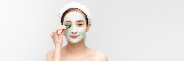 Junges Mädchen mit einer reinigenden Kosmetikmaske im Gesicht posiert mit einem grünen Blattbanner