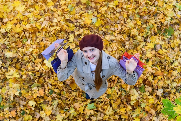 Junges Mädchen mit Einkaufstüten in den Händen auf Herbstlaub abackground Draufsicht