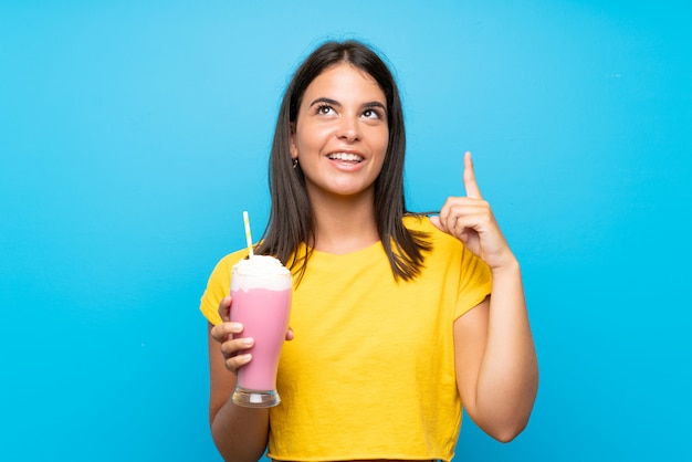 Junges Mädchen mit Erdbeermilchshake über der lokalisierten Wand, die beabsichtigt, die Lösung beim Anheben eines Fingers zu verwirklichen