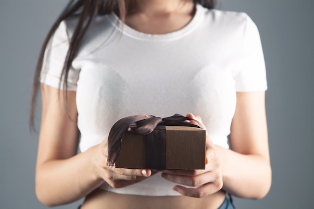 Junges Mädchen mit Geschenkbox auf grauem Hintergrund