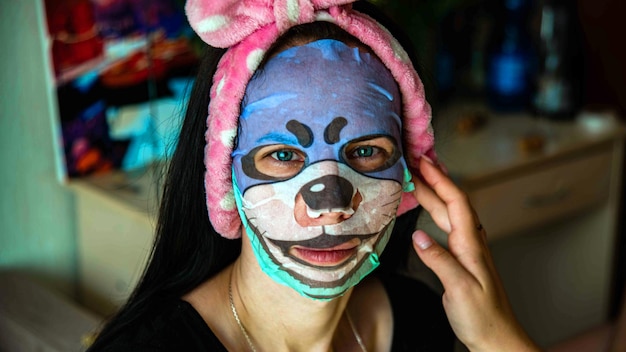 Junges Mädchen mit Gesichtsmaske, das die Kamera über dem inneren Hintergrund anschaut Kosmetisches Verfahren Beauty Spa