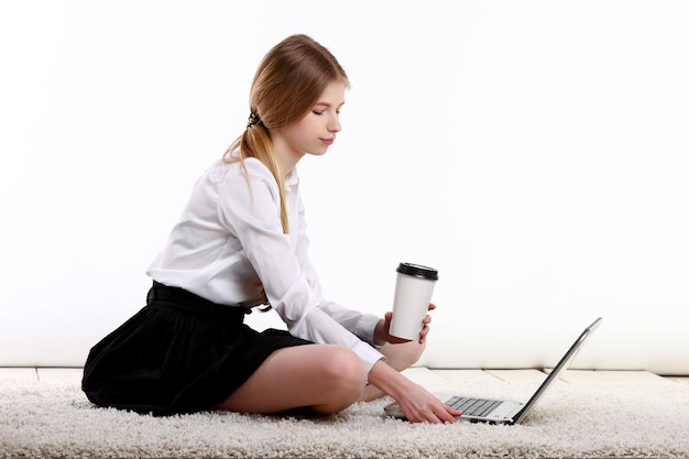 Junges Mädchen mit Kaffee sitzt auf dem Teppich mit Notebook-Computer