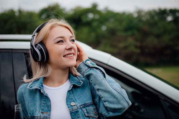 Junges Mädchen mit Kopfhörern, die Musik neben dem Auto hören